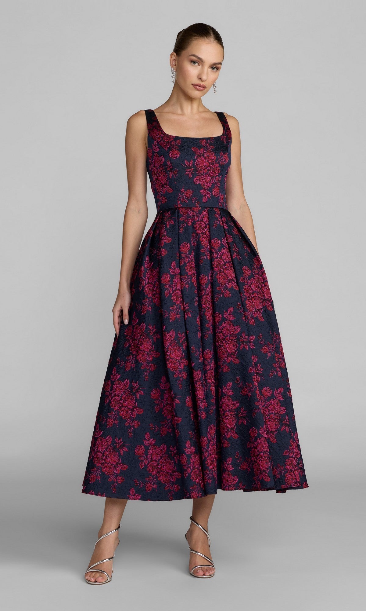 A woman wearing the Mac Duggal 68625 tea-length party dress in fuchsia multi, standing in silver strappy heels against a plain gray background.